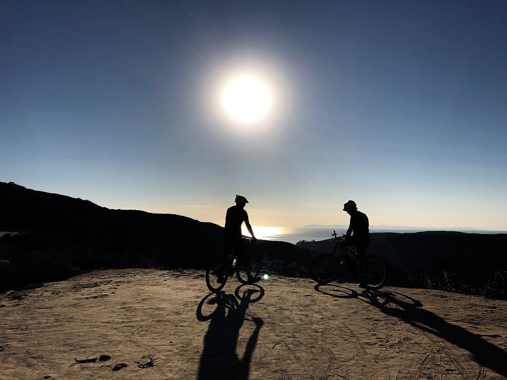 silhouette of two riders backlight by sun over ocean in Aliso Woods park. Island of Catalina in the distance.